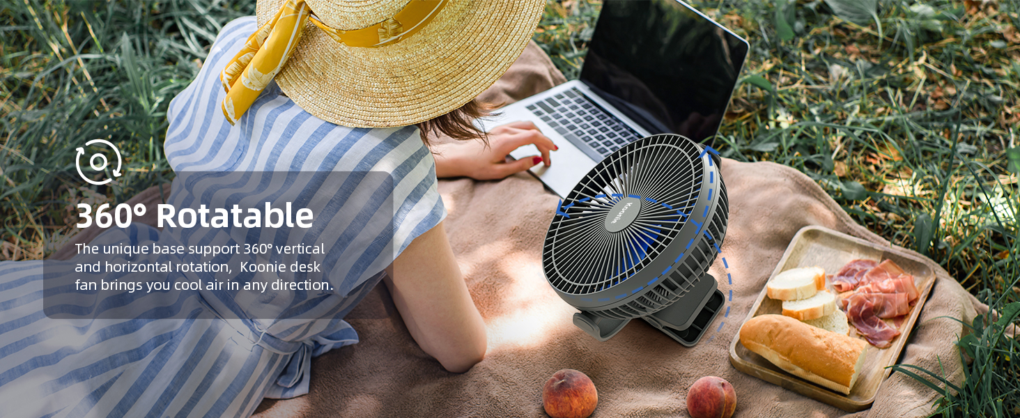 Portable fan in outdoor picnic setting. Features 360-degree rotation. Person using laptop with fan nearby, surrounded by food and straw hat.