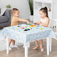 Kids playing at a table covered by light blue Disney Baby waterproof splat mat by Bumkins