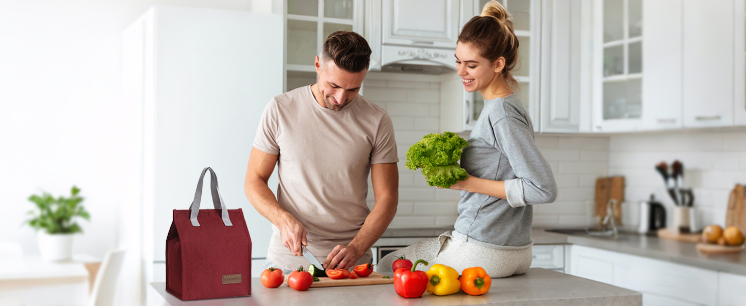 Kitchen scene showing couple preparing food on counter with fresh vegetables and burgundy tote bag visible in frame.
