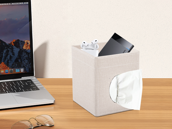 White cube-shaped tissue box holder with slot for storing electronic devices like phones or tablets on top, shown next to a laptop on wooden surface.