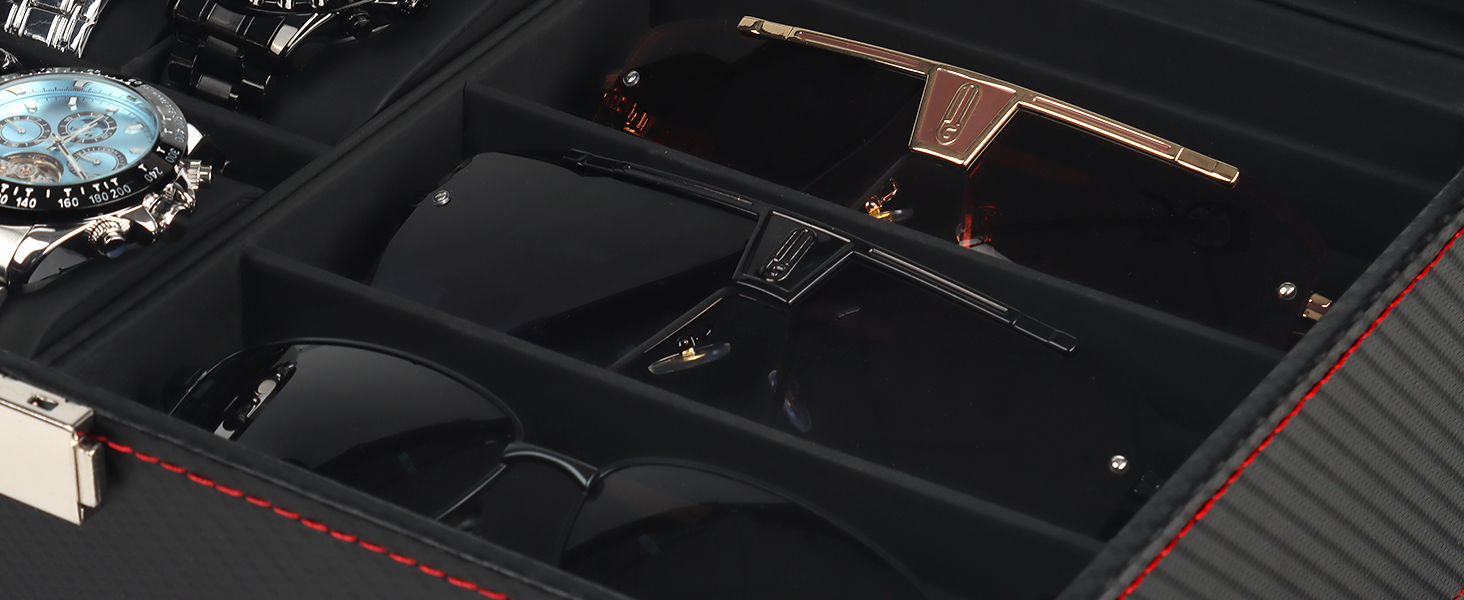 Close-up of a luxury watch case interior. Black compartments hold sunglasses, a pen, and other accessories. Red stitching and textured surfaces visible.