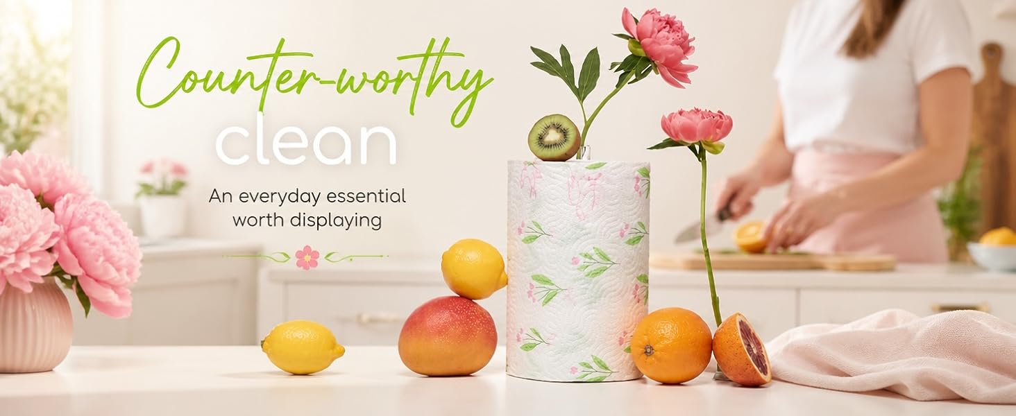Floral paper towel roll displayed on kitchen counter surrounded by fresh fruit and flowers