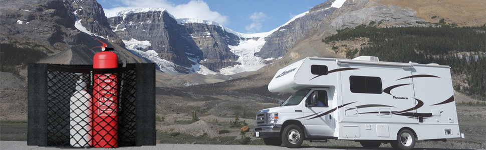 Class C motorhome parked in mountainous area. Red and black camping gear visible in foreground. Snow-capped peaks in background.