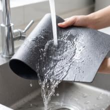 Black PU leather coffee mat rinsed under faucet, showing waterproof easy-clean surface.