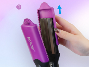 Pink hair styling tool with metal plates and 'Dyson' branding. A hand demonstrates opening the device, revealing its clamshell design. Arrow indicates direction of movement.