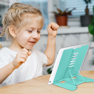 a little girl is sitting at a table with a tablet in her hand.