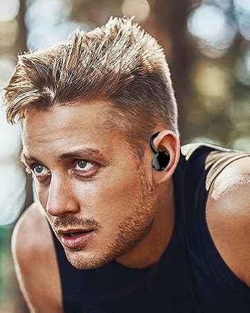Close-up of a man with short blond hair wearing a black tank top and a wireless earbud in his ear.