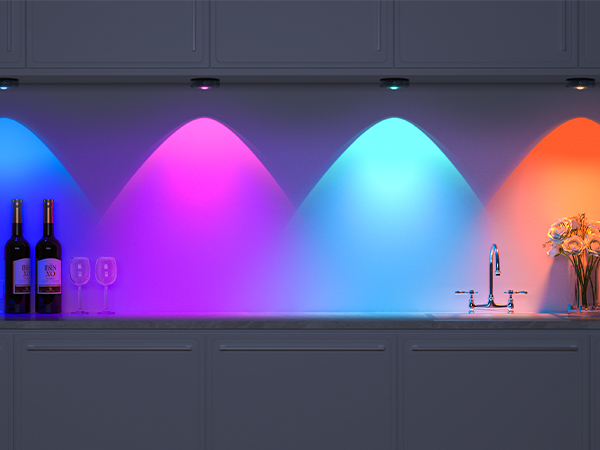 Kitchen countertop with colorful LED lighting underneath cabinets, displaying vibrant purple, pink, blue, and orange hues. Wine bottles and glasses visible.