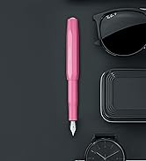 Pink fountain pen positioned against dark background with various black objects creating minimalist composition.