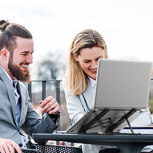 Adjustable laptop stand being used outdoors, with two people viewing screen content together. Stand appears to have multiple angle settings.