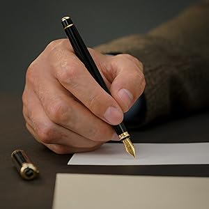 A black Scriveiner fountain pen with gold appointments resting on a piece of paper about to write
