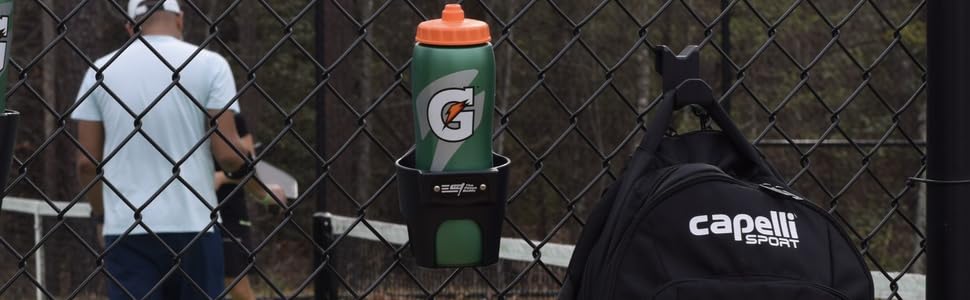 Sports bag hanging on chain link fence next to a Fence Buddy cup holder at a pickleball court