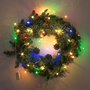 Christmas wreath with green branches and multicolored LED lights. Wreath is circular with pinecones visible among branches.