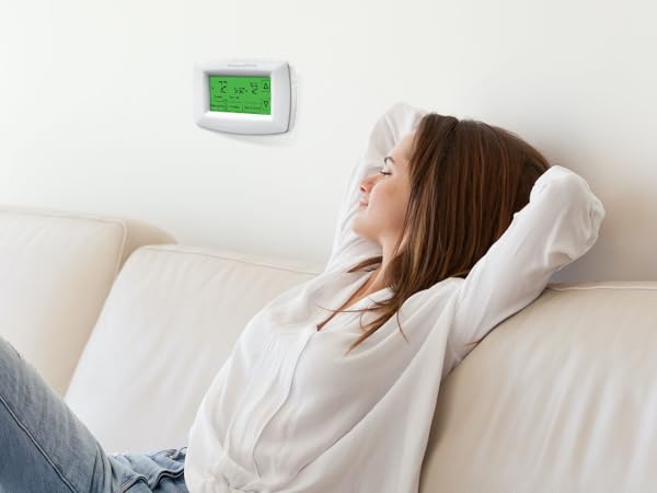 Woman relaxing on couch at home, with thermostat installed on wall behind her