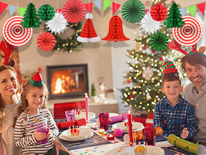 Holiday dining table setting with decorated Christmas tree, fireplace, and festive red and white decorations including hanging ornaments and table arrangements.