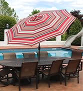 Red striped patio umbrella covering a patio table set near a large pool on an upscale patio