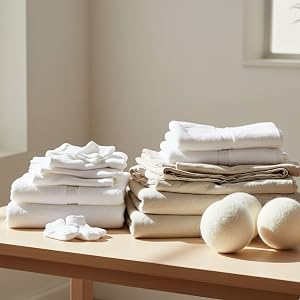 Folded white towels and tan linens arranged neatly on a wooden surface, with round white decorative objects placed between stacks.