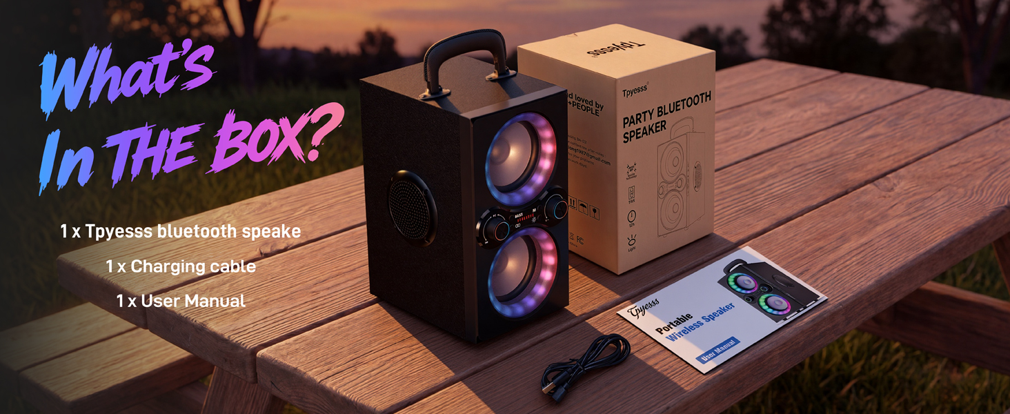 A party speaker, cardboard box, charging cable, and manual on a wooden picnic table at dusk.