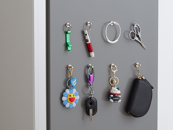 Magnetic key holder display showing various keys and accessories attached to a grey wall, including decorative keychains and small tools.