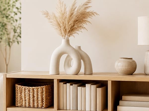 Cream ceramic donut vase with pampas grass displayed on a wooden cabinet in a warm
