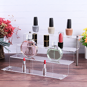 Display of fragrance bottles on clear acrylic stands with pink scattered elements in background.