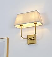 Wall-mounted brass sconce with rectangular fabric shade. Two arms support the shade, providing warm ambient lighting in a room with framed artwork.