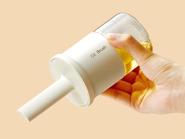 White cylindrical oil brush applicator held in hand, demonstrating use. Clear reservoir contains yellow liquid. Narrow nozzle for precise application.