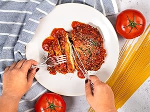 Clear knife cutting chicken parm on plate.