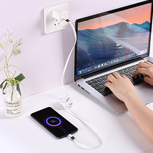 Laptop charging setup with multi-port USB charger. Person using laptop, smartphone charging, and plant in background. White USB hub plugged into wall outlet.