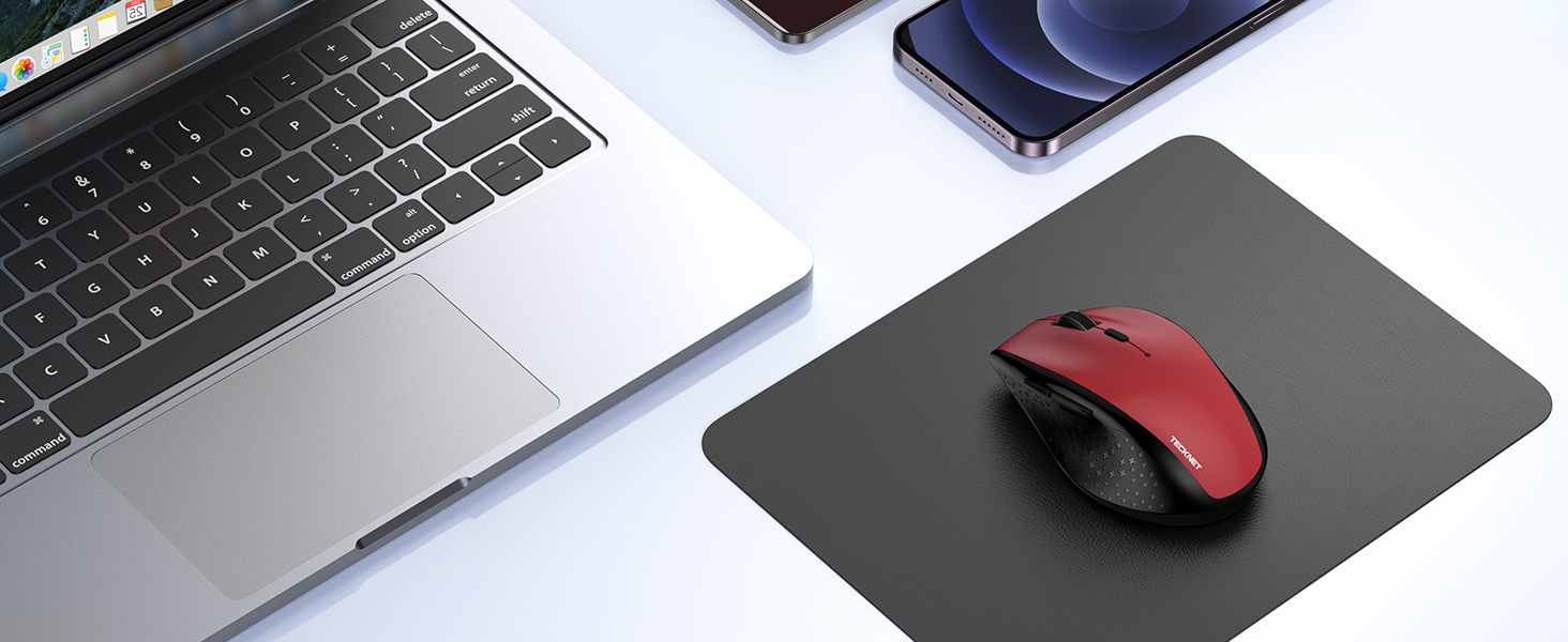 Red wireless computer mouse on a black mousepad, next to a laptop, smartphone, and part of a keyboard visible.