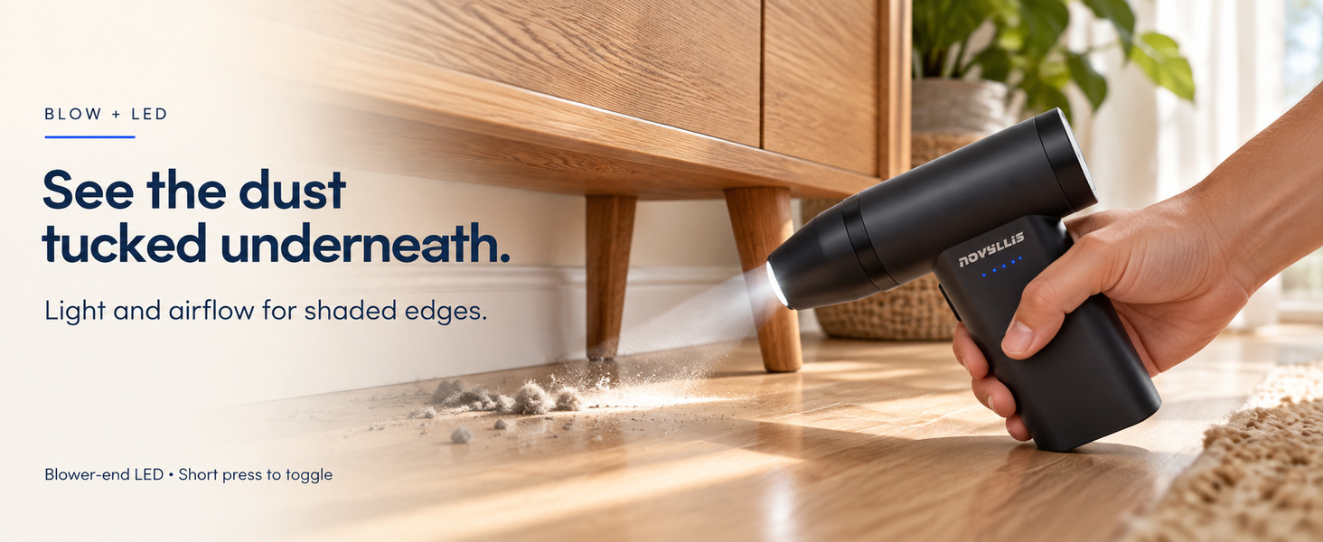 Handheld air duster with LED light illuminating loose dust beneath a wooden cabinet