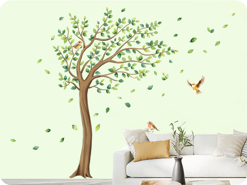 Large wall decal of a green tree with leaves and two birds. Partial view of a white couch with yellow pillow beneath the decal.