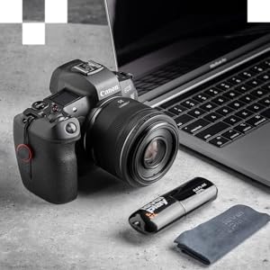 Canon DSLR camera with attached lens next to laptop, USB drive, and memory card. Camera features visible controls and prominent lens, showcasing professional photography setup.