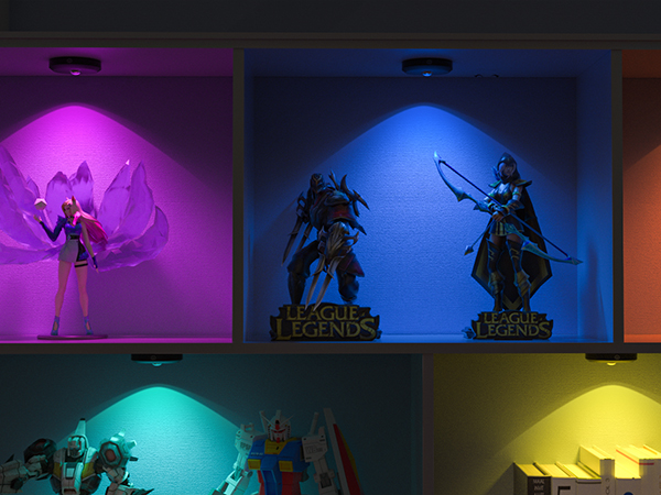 Four illuminated display cases with figurines, each lit by a different colored light: purple, blue, teal, and yellow. Text 'League of Legends' visible.