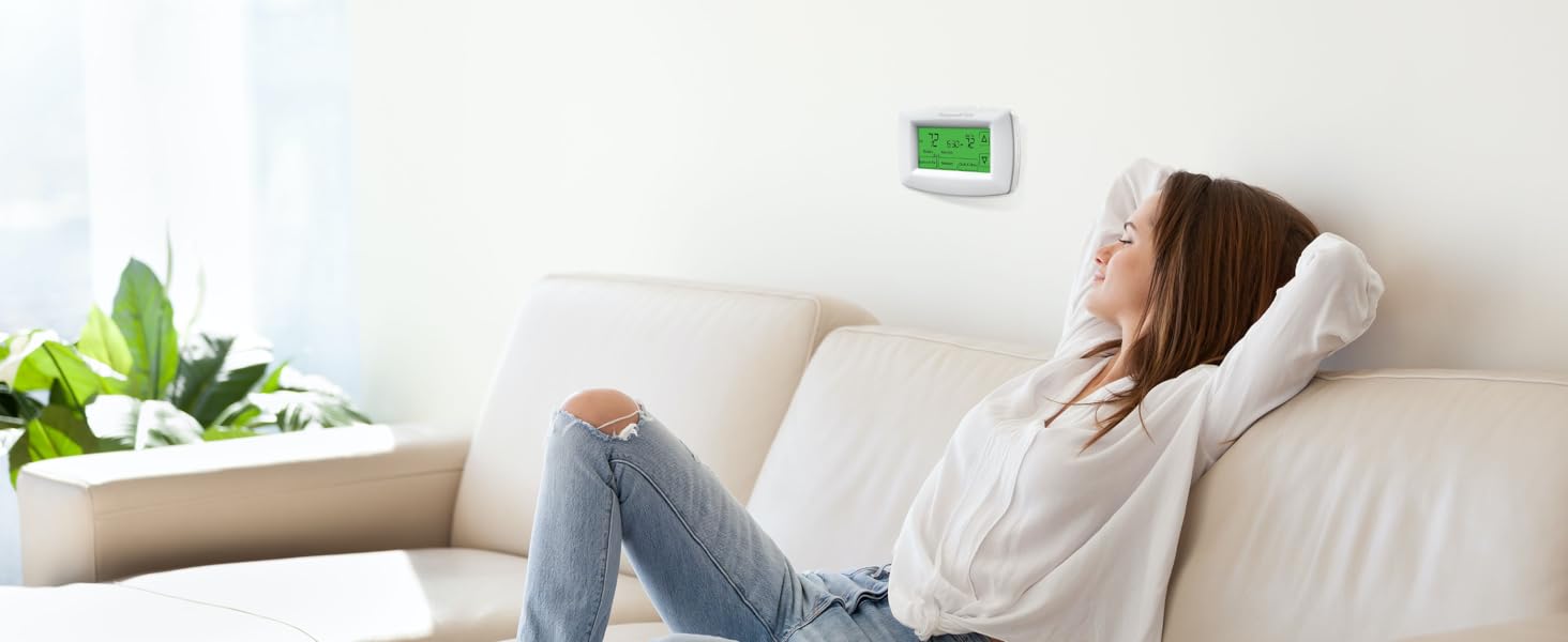 Woman relaxing on couch at home, with thermostat installed on wall behind her