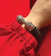 Silver bracelet with ornate beaded design worn on wrist against red fabric background.