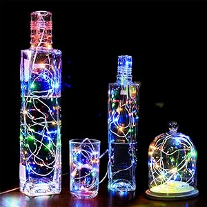 Four glass bottles and containers of varying sizes filled with colorful LED string lights, creating a luminous display against a dark background.