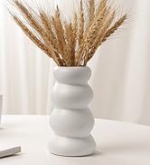 Minimalist home decor scene with white ceramic vase containing dried wheat stems, alongside rolled paper or magazine.