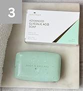 Text reads "ADVANCED GLYCOLIC ACID SOAP" and "MADE IN ENGLAND." Mint-green rectangular bar soap displayed next to white product box with teal stripe on neutral fabric.