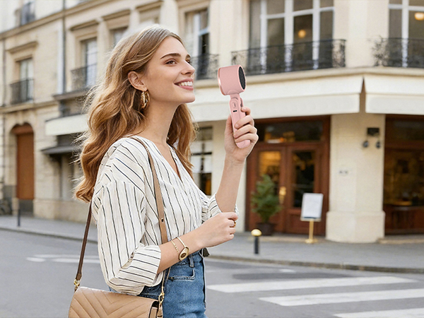 Woman walking in city holding pink handheld fan stylish mini fan for holiday travel cooling