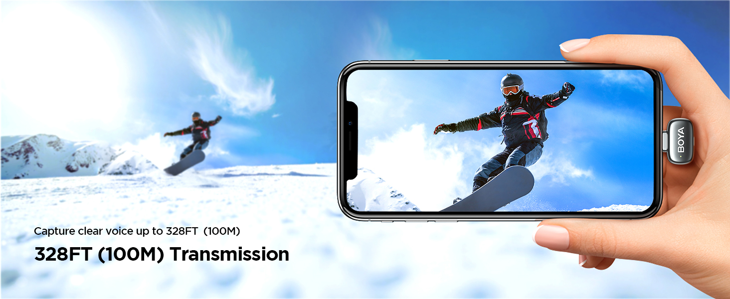 Text reads: '328FT (100M) Transmission'. Smartphone capturing action shot of snowboarder against blue sky, demonstrating camera transmission range capability.