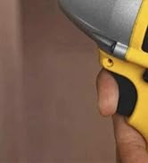 Close-up shot of a yellow and black utility knife or cutting tool being held in use position against a brown surface.