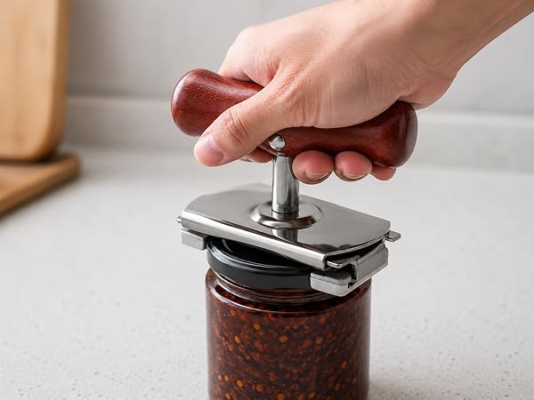 hand using wood handle jar opener on a plain unlabeled jar lid