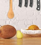 Kitchen scene with wooden spoon, knife handles, coconut, lemon, and bread in basket on wooden surface against white brick background.