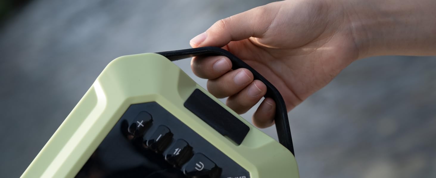 Hand holding a pale green electronic device with black buttons and a carrying handle. The device appears to be a portable control unit or measurement tool.