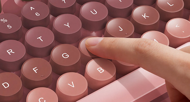 Finger pressing pink round keycaps on wireless keyboard for smooth responsive typing feel