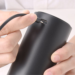 Matte black cylindrical device being held to show its curved surface and small port or button detail.