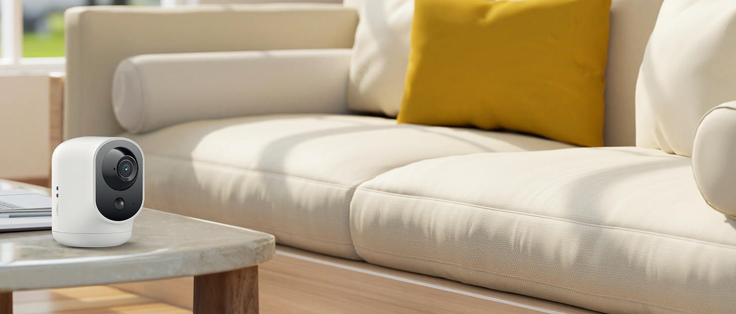 White spherical security camera on a coffee table in front of a beige couch with yellow throw pillow.