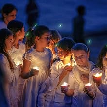 Children dressed in pure white clothes holding candles at night time