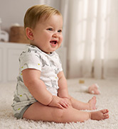happy baby boy wearing gray bodysuit illustrated with dinosaurs